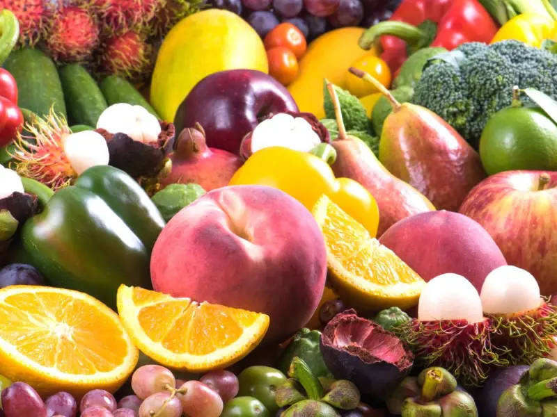 A pile of fruits and vegetables including oranges, apples, bananas, grapes, broccoli, tomatoes, and other foods.